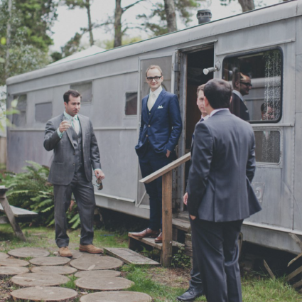 Groomsmen in suits gather on the steps of a vintage silver travel trailer